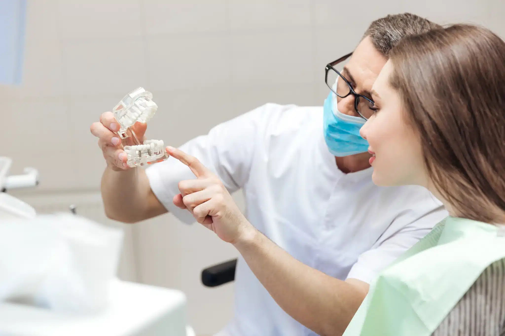 Dentist explaining dental model to female patient Happy woman sitting in dental office chair for oral surgery in fernley