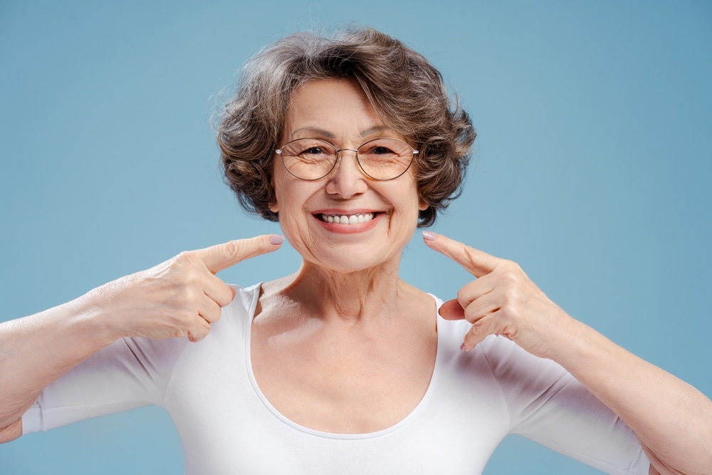 Smiling elderly woman pointing at her glasses.