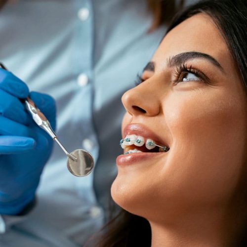 Dentist examining woman with braces using dental mirror