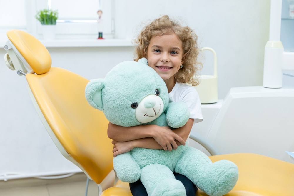 Happy girl holding teddy bear in dental office